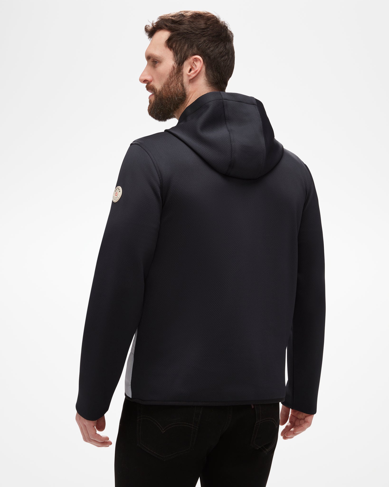 Aspen Collection Men's Aether Morgan Technical Fleece Hoodie, from the back. Black athletic fabric, patch on shoulder and large hood to protect from the elements