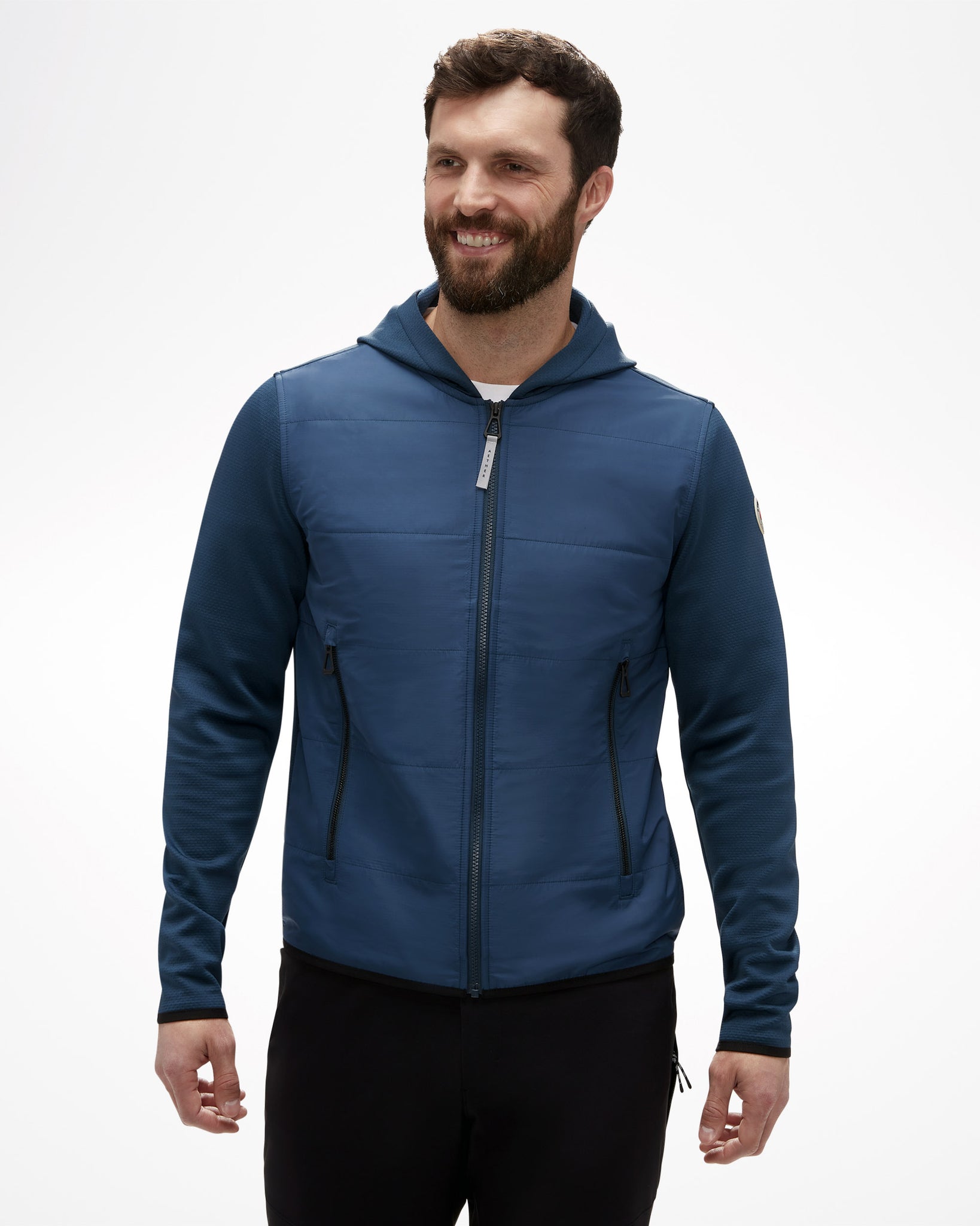 Aspen Collection men's Aether Morgan Technical Fleece Hoodie, front view of model, in blue color. Black zipper detail, vertical puff fabric on chest with athletic blue fabric on arms