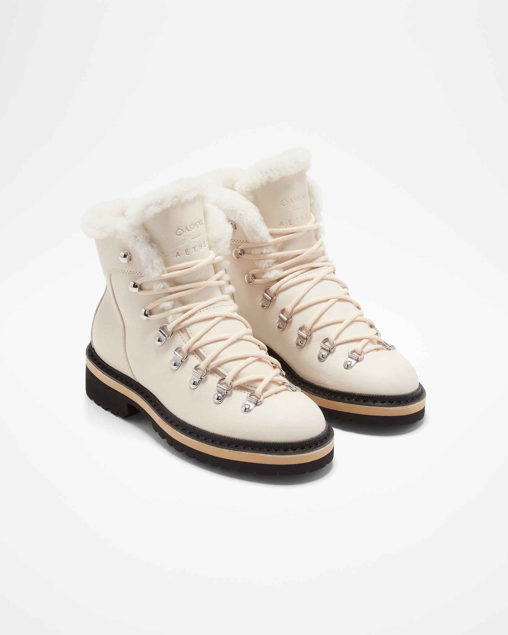 Aspen Collection Aether Dolomite Women's Shearling Boot, in white leather. Silver shoe lace cuffs, cream shoe laces. White fur lines the shoe tongue and top of boot. Black soles, small heal on boots.