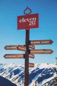 Direction pole at the Eleven212 apres venue, wood pole with red "Eleven212" sign at the top, and different peaks displayed on each directional sign