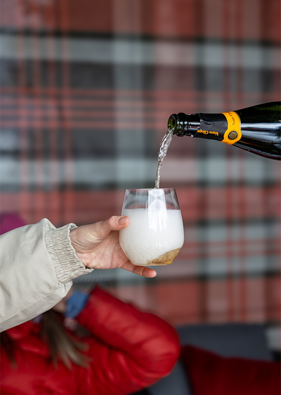 Glass is held by a hand (body out of frame) while Veuve Champagne is poured into glass