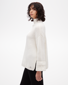 Women's Aspen Collection Cashmere Funnel Neck Sweater, loose white knit with side slit and cuffed sleeve, in all white, side view of model with small silver knit cuff on bottom corner